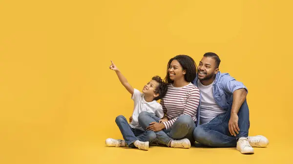 そこを見ろ コピースペース 陽気なアフリカ系アメリカ人の両親と男性の子供がイエロースタジオの背景に座って テキストを広告しながら3ポイント指の指のハッピーブラックファミリー — ストック写真