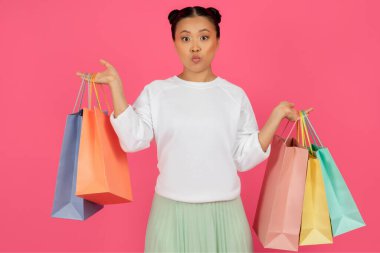 Şok olmuş Asyalı Kadın Parlak Kağıt Torbaları Tutuyor ve Kameraya Bakıyor, İnanılmaz Koreli Kadın Satın Alım Yapıyor, Pembe Stüdyo Arkaplanının Üzerinde Tek Başına Duruyor, Ücretsiz Alan