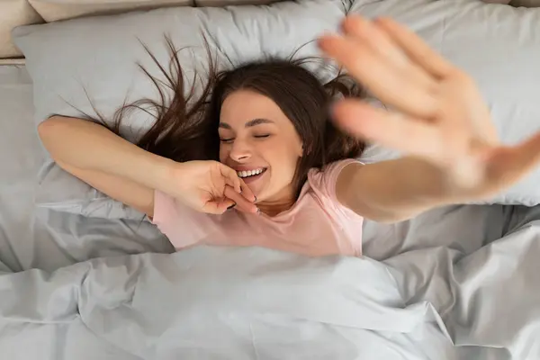 一位快乐的年轻女士躺在床上 眼睛紧闭 脸上挂着微笑 早上醒来后 她在家里尽收眼底 — 图库照片