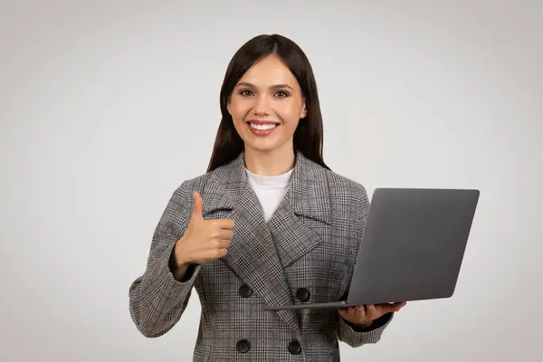 自信的职业女性手握笔记本电脑 竖起大拇指 象征着在现代商业环境中对数字解决方案的满意 — 图库照片