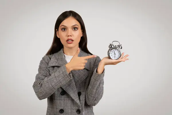Surprised Young Woman Checkered Blazer Pointing Alarm Clock Her Hand — Stock Photo, Image