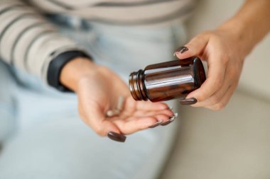 Orta Doğulu kadınların ellerine yakın çekim. Kahverengi bir şişeden avucuna ilaç dağıtırken, evdeki sağlık yönetimini, tedaviyi, kesilmiş...