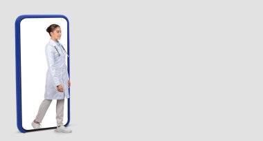 Avrupalı dengeli bir bayan doktor, dijital ve sağlık temalarını beyaz bir stüdyo arka planında, panorama üzerinde birleştirerek, sembolik bir telefon ekranı çerçevesinden gerçek dünyaya adım atıyor.