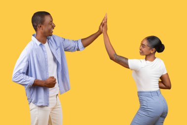 Siyah erkek ve kadın, neşeli beşlik çakar, yüzleri neşe ve dostluğu ifade eder, sarı arka plana karşı, arkadaşlığı ve başarıyı sembolize eder