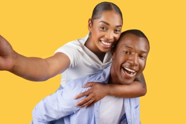 Neşeli, gülümseyen, neşeli selfie çeken, kolları açık, tek renkli sarı arka planda olan siyah bir çift.