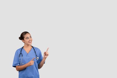 Mavili çekici bir Avrupalı doktor, olumlu bir sonuç önererek veya gri stüdyo arka planında izole edilmiş, yeni bir sağlık konsepti sunarak sevinç verici bir şekilde önlük takıyor.