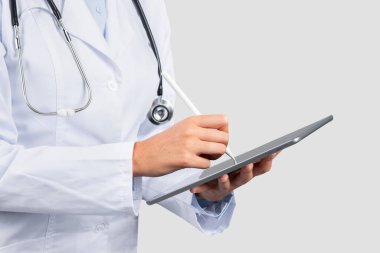 Beyaz önlüklü profesyonel Avrupalı bir kadın sağlık hizmeti sağlayıcısı modern tıbbi teknolojiyi ve hasta bakımını sembolize eden bir dijital tablet kullanıyor.