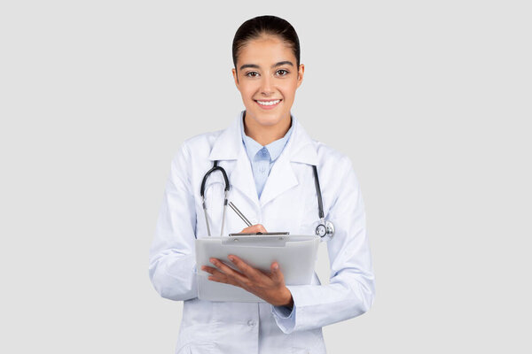 Smiling young european doctor in a white lab coat holding a tablet, looking professional and ready to engage with modern healthcare technology in a clean studio environment