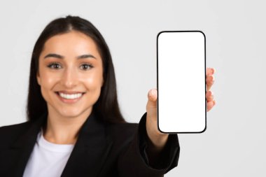 Takım elbiseli mutlu iş kadını, beyaz ekranlı akıllı telefonu gösteriyor, iş tavsiyesi, çalışma ve iş uygulaması gri arka planda izole edilmiş.