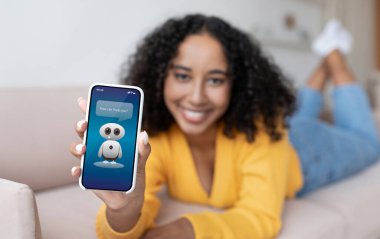 Chatbot, akıllı telefon ekranında nasıl yardımcı olabilirim? Neşeli, Afro-Amerikan kıvırcık kadın cep telefonunu internet asistanı Savescreen ile gösteriyor, evde takılıyor.