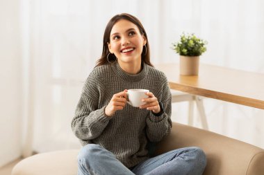 Çekici beyaz kadın oturma odasında kahvesini yudumlayarak tembellik ediyor, fotokopi çekiyor. Güzel, genç, esmer bir bayan evinde bir fincan sıcak içecekle kanepede dinleniyor.