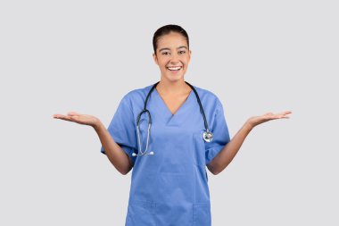 Mavi üniformalı mutlu beyaz kadın doktor hemşire ellerinde fotokopi odası, gri stüdyo arka planında izole. Tıbbi reklam ve teklif, satış, soru, sağlık hizmeti seçimi.