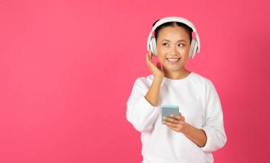 Müzik uygulaması. Neşeli Asyalı Kadın, Smartphone ve kablosuz kulaklıklarla en sevdiği şarkıları dinliyor, Mutlu Gülümseyen Koreli Kadın, Pembe Stüdyo Arkaplanına Karşı Duruyor, Kopya Alanı