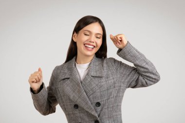 Kareli ceketli ışıl ışıl genç bir bayan gözleri kapalı dans etmekten zevk alıyor ve büyük bir gülümseme, saf neşe ve tasasız bir tutum sergiliyor.