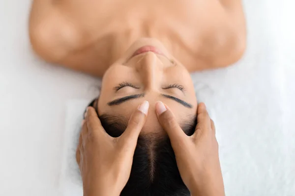 A serene half-naked brunette young hindu lady lies in repose during a professional head massage, a moment of zen in a luxurious spa atmosphere, top view