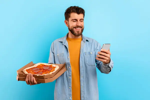 Hungry Young Man Holding Pizza Box Using Smartphone Standing Blue — Stock Photo, Image