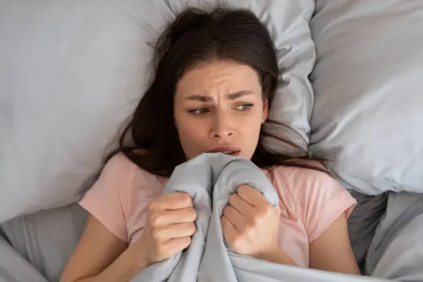 惊慌失措的年轻女子躺在床上害怕声响 或者睡不着觉 把毛毯拉到家里 高瞻远瞩 焦虑和失眠 — 图库照片