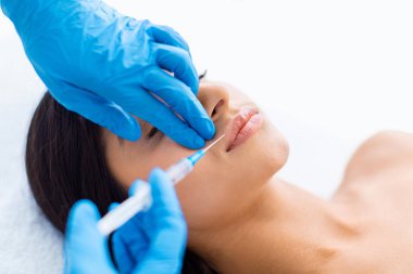 Klinikte dudak dolgusu yaptıran Hintli genç ve güzel bir kadının yakın çekimi. SPA merkezinde güzel bir bayan için hyaluronik asit enjeksiyonu yapan doktor elleri.