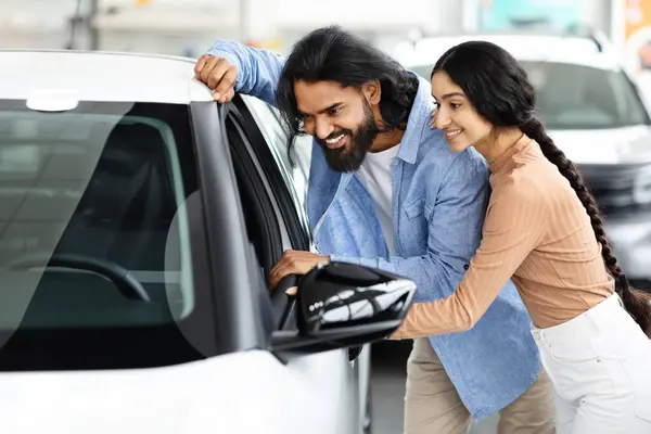 Choosing Auto. Happy Indian Spouses Looking Inside Of Their New Car Together, Checking Interior And Characteristics Of Vehicle While Purchasing Auto In Modern Dealership Center, Closeup Shot