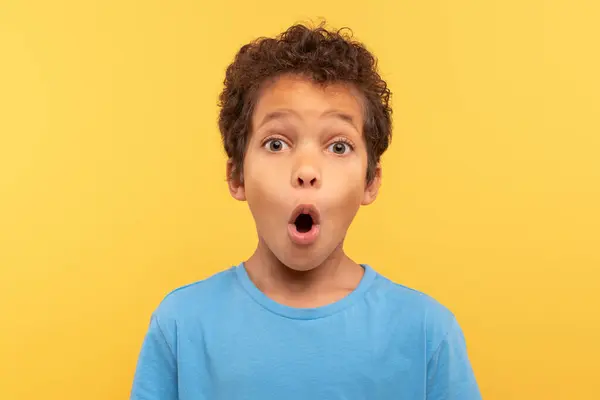 カーリーヘアの驚異的な若い少年 驚きの口の形 明白な黄色の背景に対して軽い青いシャツを身に着け 驚きの瞬間をキャプチャする — ストック写真