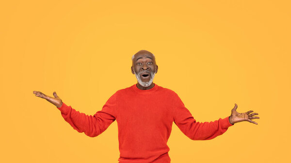 Радостный африканский пожилой человек в ярком красном свитере и одинаковой шляпе широко раскрывает руки с удивлением и восторгом на солнечном желтом фоне студии, панорама