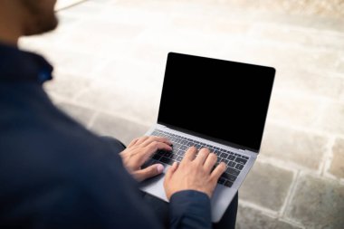 Tanımlanamayan genç işadamının laptopta siyah boş ekran ile yazarken çekilmiş görüntüleri, şehir merkezinde otururken, web sitesi reklamları ve çevrimiçi iş teklifleri için model alınırken.