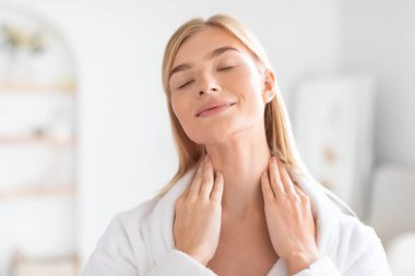 Çekici sarışın bayan nazikçe boynuna nemlendirici sürüyor. Güzelliği ve kendine özgüveni somutlaştırıyor. Güzellik ayini sırasında boynuna masaj yapıyor.