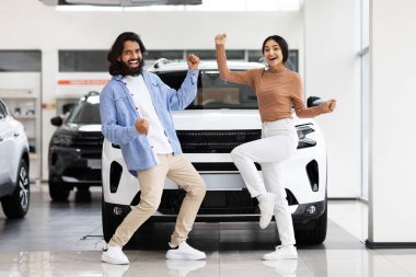 İlk aile arabası. Mutlu genç Hintli çift, galeriden yeni bir araba aldıktan sonra el sıkışıyor ve dans ediyor. Milenyum eşleri galeride modern araç satın alımını kutluyorlar