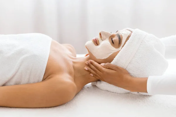 Captured in a soothing setting, young indian woman enjoys a premium facial mask and relaxing neck massage at luxury spa center environment. Full body beauty treatment, side view