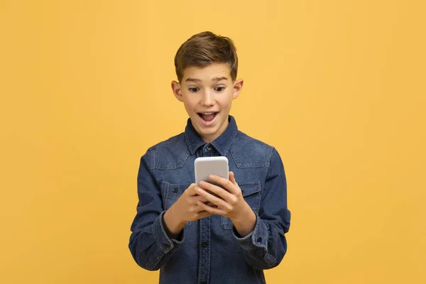 モバイルオファー 興奮とスマートフォン画面を見ている楽しい10代の少年は 感情的に良いニュースに反応し 黄色いスタジオの背景に口を開いたまま スペースをコピー — ストック写真