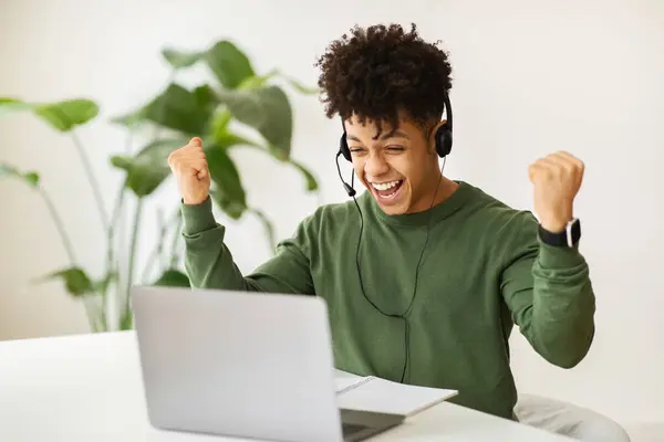 Excited black guy remote employee working at cafe, using headset and computer laptop, raising hands up and exclaiming, celebrating success. Career opportunities, distant job, freelance