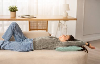 Rahat genç bir kadının kanepeye uzanmış, gözleri kapalı, vücudunu esnetirken, evde tembelce hafta sonunun keyfini çıkarırken yan görüntüsü. Stres atma, dinlenme, rahatlama konsepti, kopyalama alanı