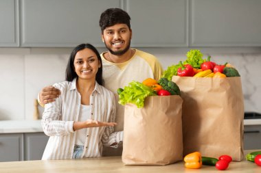 Çevrimiçi market teslimatı. Sevgi dolu Hintli çift alışverişlerini marketten gösteriyorlar taze organik meyve ve sebzelerle dolu poşetlerden, mutfakta kucaklaşıyorlar. Sağlıklı gıda, beslenme