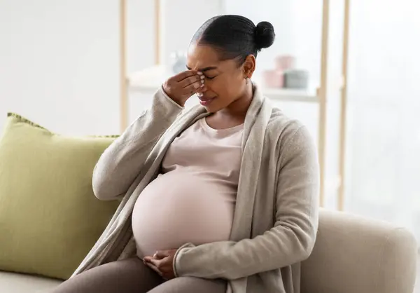頭痛や片頭痛に苦しむ若い妊娠中のアフリカ系アメリカ人女性 病気を感じる ソファに座って 彼女の大きな腫れに触れ 鼻の橋をこすり 空きスペース — ストック写真
