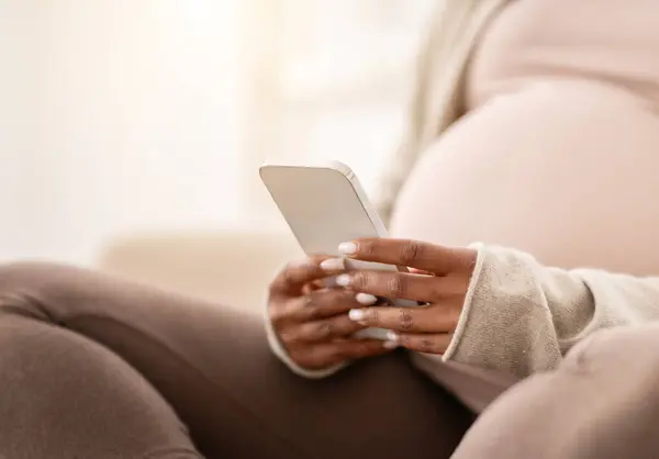 怀孕的黑人女人坐在沙发上用智能手机拍的照片准妈妈带着怀孕跟踪应用程序的手机 复制空间 — 图库照片