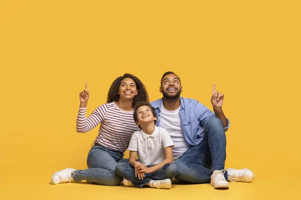 彼らの頭の上のコピースペースで3ポイントアップのハッピーブラックファミリー あなたのデザインのための黄色の背景の上に空の場所を示す幸せなアフリカ系アメリカ人の両親と男性の子供デモンストレーション — ストック写真