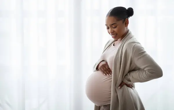 感受到与未出生孩子的联系 快乐的怀孕年轻黑人女人摸着她的肚子 白色的窗户背景与空旷的空间 — 图库照片
