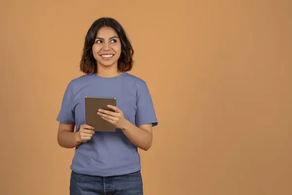 素敵なモバイルアプリ オンラインオファーや取引をチェックする彼女の手のデジタルタブレットを持つポジティブな若いアラブ女性 茶色の背景で孤立した広告のコピースペースを見て パノラマ — ストック写真