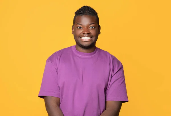 身穿紫色T恤衫的全黑男子在黄色背景下对着相机微笑 工作室拍摄 正面的非洲裔美国年轻人随意表达正面情感的肖像 — 图库照片