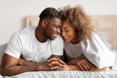 Afro-Amerikalı genç çiftin el ele tutuşması, alınlarına dokunması, rahat bir yatakta kucaklaşması ve flört etmesi, sabah yatak odasının iç kısmında samimiyet ve romantizmin tadını çıkarması.