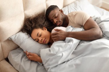 Sıcak bir sabah. Genç siyahi çift, evlerinde, aile yatağında birlikte uyurlarken, sağlıklı uyku ve dinlenme rutininin keyfini çıkarırken, modern yatak odasında uyurlarken.