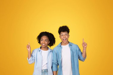 İki heyecanlı Afro-Amerikalı genç yetişkin, parlak tebessümleriyle yukarı çıkıyorlar, parlak sarı bir arka plana karşı duruyorlar, keşif ve coşku duygusu ile