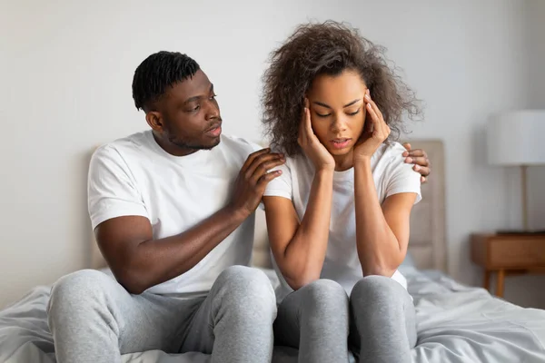 Supportive millennial black husband comforting and supporting his depressed wife in moment of despair in bedroom, hugging woman and saying good words. Relationship challenges concept
