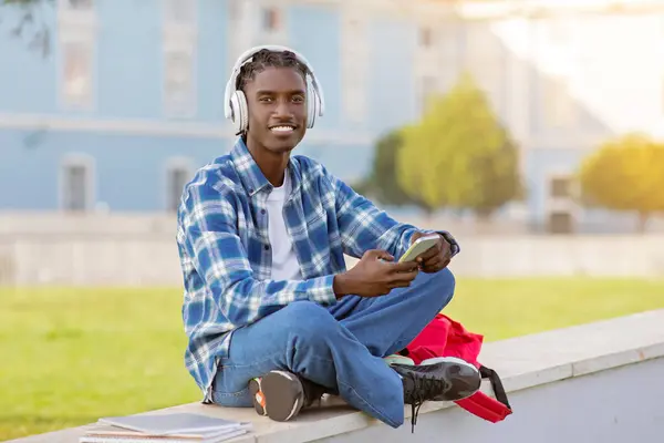 Szczęśliwy Zrelaksowany Czarny Student Facet Bezprzewodowymi Słuchawkami Przegląda Smartfon Dla — Zdjęcie stockowe