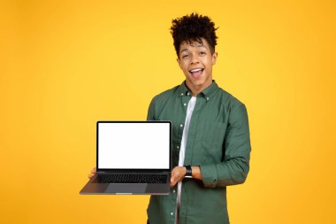 Duygusal genç siyah adam elinde beyaz ekranlı modern bilgisayar dizüstü bilgisayarını tutuyor ve sarı stüdyo arka planında izole edilmiş olduğunu haykırıyor. Heyecan verici teklif, taklit, kopyalama alanı.
