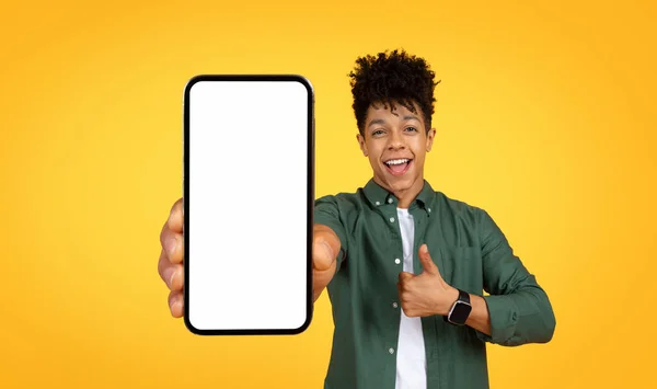 快乐英俊的非洲裔美国年轻人 拿着白色的空白屏幕展示大手机 摆出大拇指的架势 推荐网上报价 黄色工作室背景 复制空间 — 图库照片
