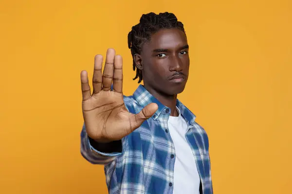 No Discrimination. Portrait Of Serious Young Black Man Showing Stop Gesture At Camera, Millennial African American Guy Standing With Outstretched Hand, Isolated Over Yellow Background, Copy Space