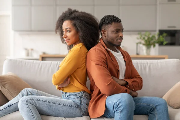 Relationships Problem. Frustrated African American Couple Sulking After Quarrel, Thinking About Breakup Sitting On Couch Back To Back In Modern Living Room. Indifference, Family Conflict