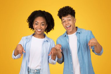 Mutlu Afro-Amerikan genç kadın ve erkek doğrudan kameraya bakıyor, izleyicileri katılmaya davet ediyor, açık sarı bir arkaplana karşı.