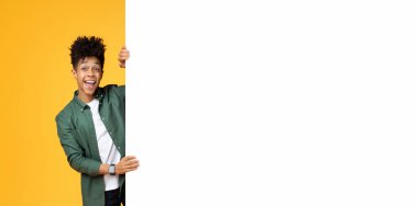 Bin yıllık olumlu siyahi adam beyaz boş reklam panosunun yanında duruyor metin veya reklam için kopya alanı, sarı stüdyo arka planı, web-afişi